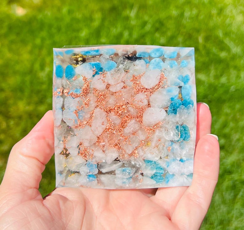 K&ouml;nnte beinhalten: Ein quadratisches Kristallgitter mit einer klaren Harzbasis. Das Gitter ist mit kleinen wei&szlig;en, blauen und kupferfarbenen Kristallen gef&uuml;llt.