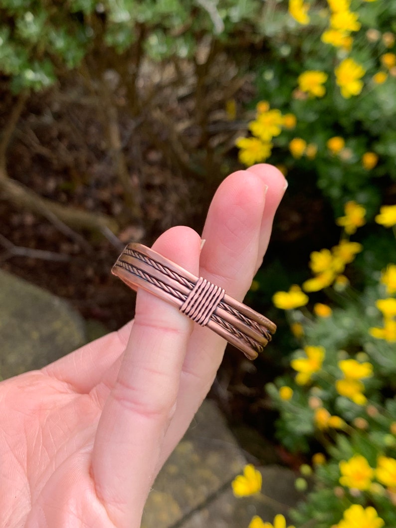 Op de afbeelding: Een koperen draadring met een gevlochten ontwerp. De ring wordt aan een vinger gedragen.
