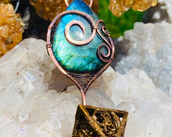 May include: A copper wire wrapped pendant featuring a teardrop-shaped blue labradorite gemstone and a geometric, ornate, gold-toned metal cage.