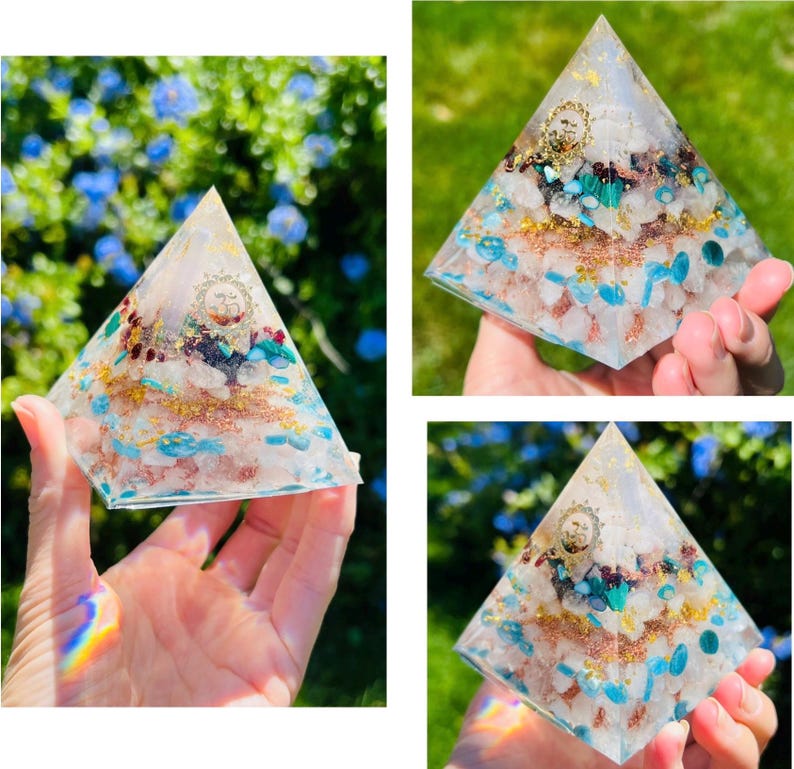 K&ouml;nnte beinhalten: Eine klare Kristallpyramide mit einer Vielzahl von Kristallen und Goldflocken, die darin eingebettet sind. Die Pyramide ist etwa 7,5 cm hoch und steht auf einer Hand.