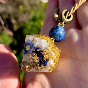 May include: A gold chain necklace with a clear resin pendant containing blue and gold flecks. The pendant is attached to a blue bead.