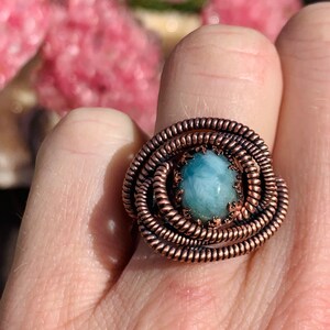 May include: A copper wire wrapped ring with a light blue oval gemstone in the center.
