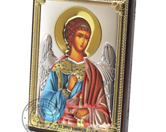 May include: A silver and gold icon of the Archangel Michael with a blue robe, red cloak, and a sword. The icon is framed in a dark wood frame with a gold trim.