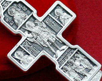 May include: A silver Orthodox cross with intricate details. The cross features multiple figures, including an angel with wings and a sword, and the text "ЗАЩИТНИК ХРИСТИАНСКИЙ ЗВЕРЬ" (Defender of Christians, Beast).