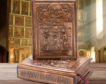 May include: Two antique-looking, copper-colored prayer books with embossed religious imagery. The top book features a depiction of Jesus on the cross with two figures flanking him. The bottom book has the word "МОЛИТВОСЛОВ" embossed on the cover.