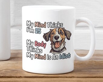 May include: White ceramic coffee mug with a cartoon dog and the text "My Mind Thinks I'm 25 My Body Thinks My Mind Is An Idiot"