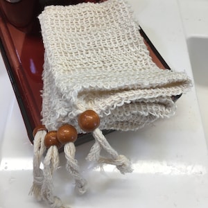 May include: A white, crocheted washcloth with wooden beads and knotted ties. The washcloth is folded and sitting on a red surface.
