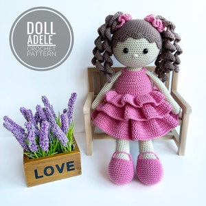 Puede incluir: Muñeca de crochet con cabello castaño en coletas, vistiendo un vestido rosa y zapatos rosas. La muñeca está sentada en un banco de madera con una planta en maceta con flores moradas que dice "LOVE" en el lateral. El texto "DOLL ADELE CROCHET PATTERN" está en un círculo sobre la muñeca.