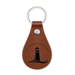 May include: A brown leather keychain with a silver key ring. The keychain features a black silhouette of a lighthouse above a wavy line. A silver snap secures the leather loop to the key ring.