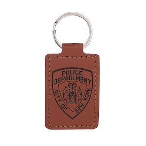 May include: A brown leather keychain with a silver key ring. The rectangular tag features the words "POLICE DEPARTMENT CITY OF NEW YORK" around a shield emblem.