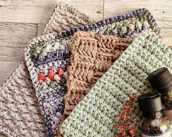 May include: Four crocheted squares in different colours and patterns, including beige, green, brown, and purple. The squares are stacked on top of each other. Two small glass jars with labels are in the bottom right corner of the image.