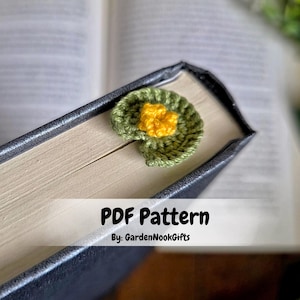 以下が含まれることがあります： 黄色い花の真ん中がある、手作りのかぎ針編みのスイレンの葉の形をしたブックマーク。緑と黄色のブックマークは本のページに置かれています。画像には「PDF Pattern By: GardenNookGifts」というテキストが含まれています。