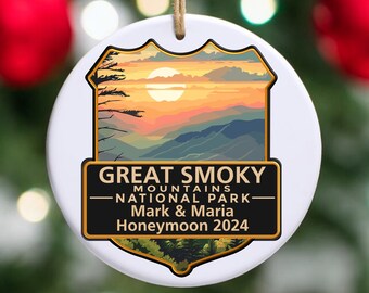 May include: White ceramic ornament with a sunset scene of the Great Smoky Mountains National Park. The text reads "Great Smoky Mountains National Park" and "Mark & Maria Honeymoon 2024".