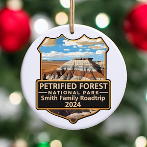 May include: White ceramic ornament with a colorful image of Petrified Forest National Park. The ornament has a gold border and the text "Petrified Forest National Park - Smith Family Roadtrip 2024".