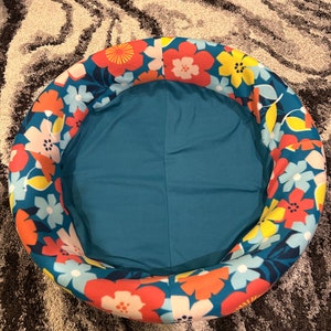 May include: A round, inflatable pool with a floral print in shades of red, yellow, blue, and white. The pool is deflated and sitting on a gray and white rug.