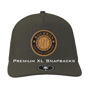 May include: Olive green snapback hat with a circular logo featuring a wooden barrel design and the words "BOURBON LEATHER COMPANY". The text "PREMIUM XL SNAPBACKS" is printed below the logo.