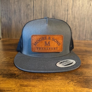 May include: A gray and black trucker hat with a brown leather patch that says "Moore & Sons M Transport".
