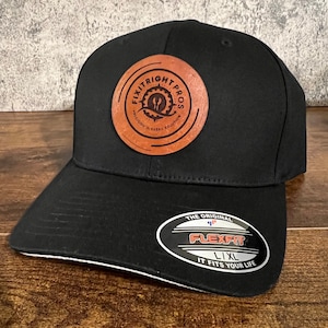 May include: Black baseball cap with a brown leather patch that says "Fixitright Pros Precision in Every Solution". The cap has a white underbrim and a Flexfit label that says "The Original Flexfit L/XL It Fits Your Life".