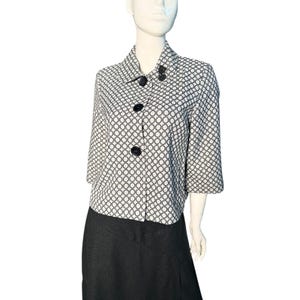 Peut inclure: Veste à motifs noir et blanc avec trois gros boutons noirs. La veste a des manches trois-quarts et un col. Elle est associée à une jupe noire. Le motif est un motif circulaire répétitif.