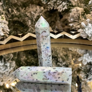 Peut inclure: Deux pointes de cristal irisées blanches et grises avec un motif moucheté. Les pointes sont posées sur une surface réfléchissante.