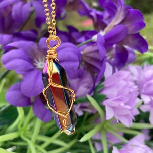May include: A gold chain necklace with an iridescent crystal pendant wrapped in gold wire. The pendant is a long, pointed shape with a rainbow of colours.