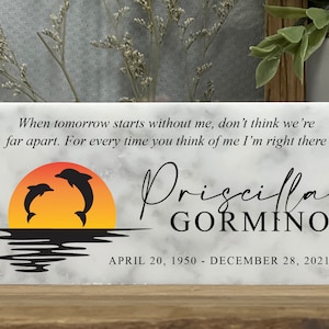 May include: A white marble memorial plaque with a quote about remembering someone who has passed away. The quote reads "When tomorrow starts without me, don't think we're far apart. For every time you think of me I'm right there." The plaque also features a silhouette of two dolphins jumping over a sunset. The name "Priscilla GORMINO" is written in cursive script below the sunset. The dates "APRIL 20, 1950 - DECEMBER 28, 2021" are printed below the name.