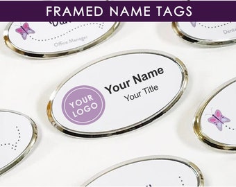 Puede incluir: Etiquetas de nombre ovaladas con marco plateado y diseño de mariposa. Las etiquetas tienen un fondo blanco y un logotipo morado que dice "YOUR LOGO". El texto "Your Name" y "Your Title" está impreso en la etiqueta.
