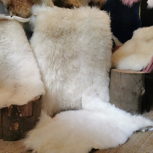 Puede incluir: Cuatro alfombras de piel de oveja blanca expuestas sobre una superficie de madera. Las alfombras son suaves y esponjosas, perfectas para añadir calidez y textura a cualquier habitación.