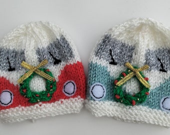 May include: Two knitted hats shaped like a Christmas-themed camper van. One hat is red and white with a green wreath, the other is blue and white with a green wreath.