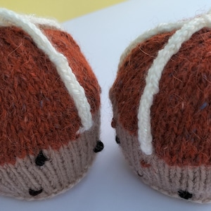 Puede incluir: Dos objetos redondos de punto de color marrón y blanco con un patrón de cruz blanca en la parte superior. Los objetos están hechos de hilo y tienen una combinación de colores marrón y blanco.