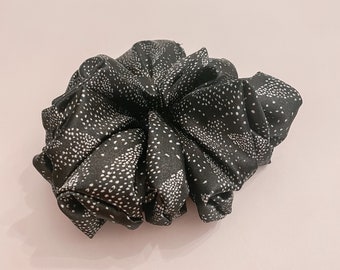 May include: Black and white patterned scrunchie made of fabric. The scrunchie is in the shape of a flower.
