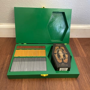 Pu&ograve; includere: Una scatola di legno verde con chiusura dorata, aperta per rivelare carte da gioco di vari colori e una scatola di carte a forma di bara. La scatola a bara ha la parola "SRENCC".
