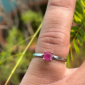 Op de afbeelding: Een zilveren ring met een vierkante roze edelsteen.