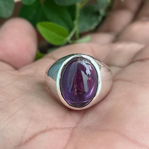 May include: A silver ring featuring a large, oval amethyst gemstone. The ring has a simple, classic design.
