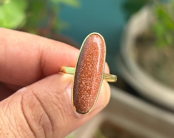 May include: A gold ring with a brown oval-shaped gemstone. The gemstone has a speckled texture.