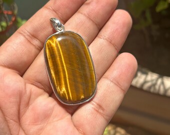 May include: A silver pendant with a large oval-shaped tiger's eye gemstone. The gemstone is a rich brown color with golden streaks.