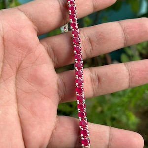 Pode incluir: Um bracelete de ténis de prata com uma fila de pedras redondas vermelhas.
