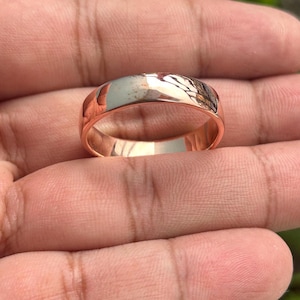 May include: A simple, polished, rose gold wedding band.