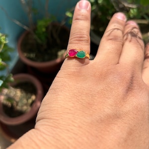 May include: A gold ring with a red and green gemstone setting. The ring is on a person's finger.