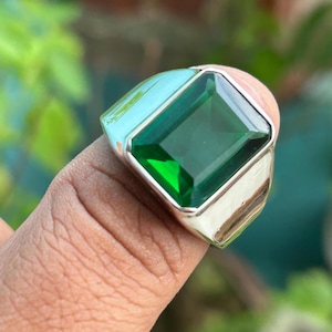 May include: A silver ring featuring a large, emerald green gemstone. The gemstone is cut in a rectangular shape with bevelled edges.