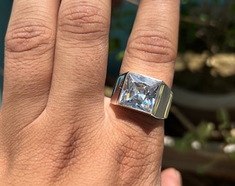 May include: A silver ring with a large, clear square-shaped gemstone.