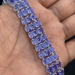 Può includere: Un bracciale a più file composto da numerose pietre preziose tanzanite di colore blu-viola vibrante, con taglio ovale e incastonate in griffe di metallo color argento. Il design presenta tre file parallele di pietre sfaccettate a maglie.