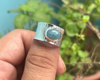May include: A silver ring with a textured band and a light blue oval gemstone.