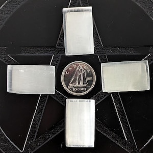 May include: Four rectangular selenite crystals arranged in a cross shape on a black background with a Canadian 10-cent coin in the centre.