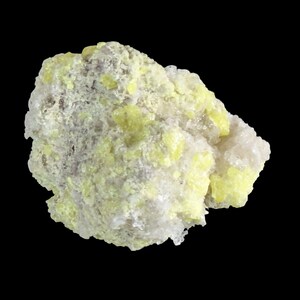 Op de afbeelding: Een close-up van een mineraal specimen tegen een zwarte achtergrond. De rotsformatie heeft een mix van lichtgele, witte en grijze kleuren. De textuur lijkt ruw en kristallijn, met zichtbare minerale afzettingen.