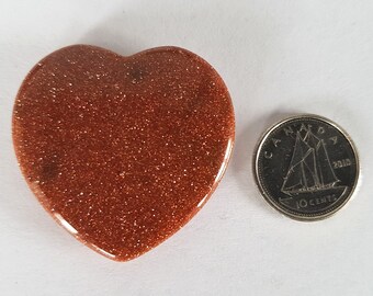 May include: A heart-shaped polished stone with a reddish-brown color and a sparkly texture. The stone is about the size of a Canadian dime.