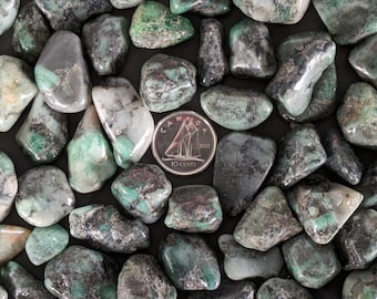 May include: A collection of tumbled emerald green stones with black and white inclusions. The stones are various sizes and shapes, and are arranged on a black surface. A Canadian 10-cent coin is included for scale.