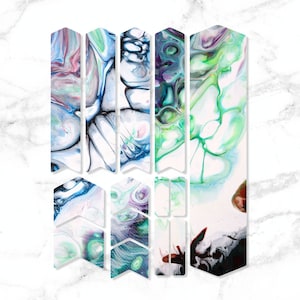 May include: A set of 10 colourful abstract arrow-shaped stickers with a white background. The stickers feature a swirling, marbled pattern in shades of blue, green, pink, and black.