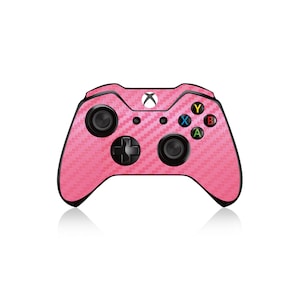 Może przedstawiać: Różowy kontroler Xbox z wzorem imitującym włókno węglowe. Kontroler ma czarne przyciski i czarny krzyż kierunkowy.