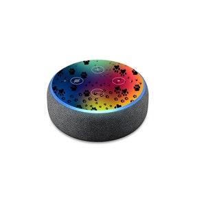 May include: A black and gray smart speaker with a rainbow and black paw print design. The speaker has a blue light ring around the top.